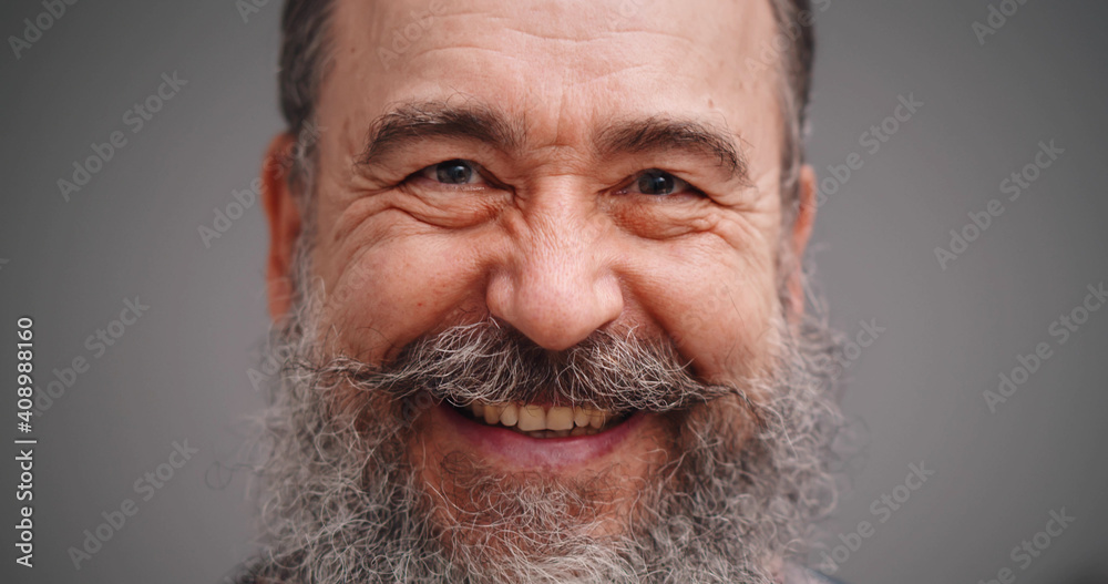 Portrait of positive bearded elderly man smiling isolated on gray background