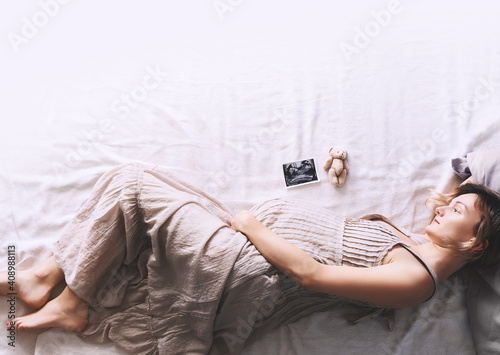 Pregnant woman in dress holding hands on belly lying on side in profile in bed.  Expectant mother waiting for baby birth during pregnancy. photo