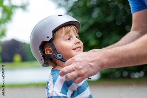 Father puts a safety helmet on little smiling boy for scooter ,cycling and rollerblading in the park. child safety on the playground