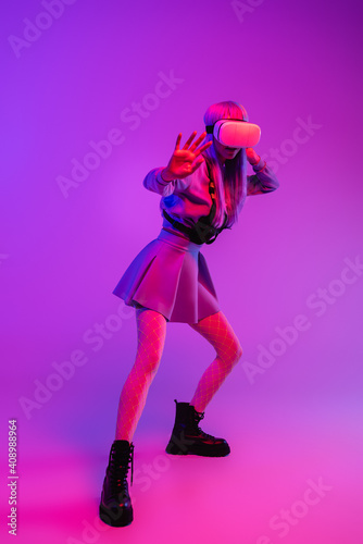 full length of young woman in virtual reality headset standing with outstretched hand on purple background