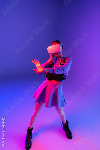 full length of young woman in virtual reality headset gesturing on purple background