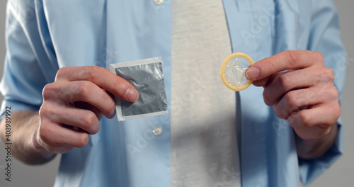 Close up of man holding unwrapped condom in hand standing isolated on grey background