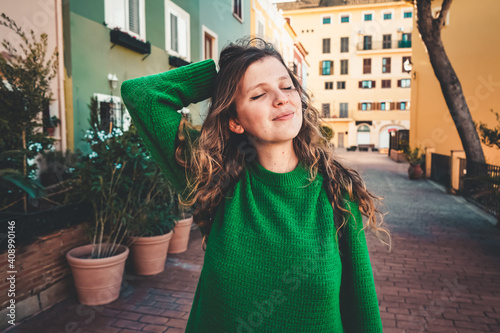 Young woman wearing green oversize sweater enjoying a windy day in a colorful city photo