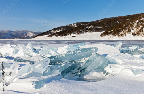 Beautiful winter landscape of frozen Lake Baikal on sunny January day. Snowy ice hummocks with transparent blue piles of ice near the village of Bolshoye Goloustnoye. Natural background. Winter travel
