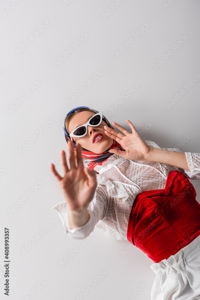 high angle view of trendy woman in headscarf and sunglasses lying while gesturing on white high angle view of trendy woman in headscarf and sunglasses lying while gesturing on white