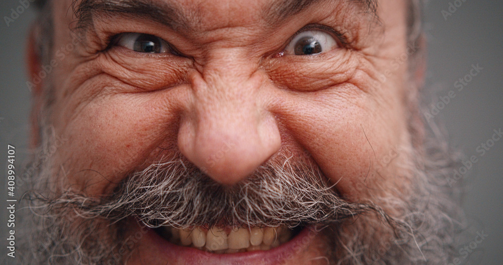 Close up portrait of bearded senior man with crazy grimace isolated on gray background