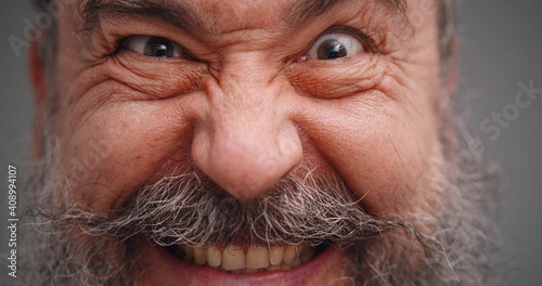 Close up portrait of bearded senior man with crazy grimace isolated on gray background