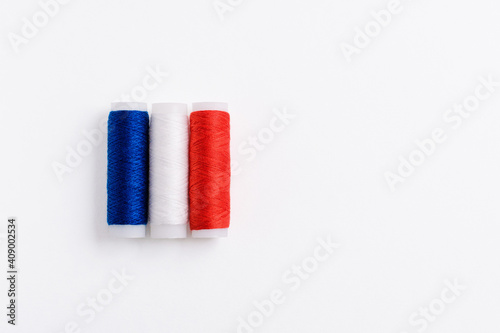 Three spools of thread for sewing are stacked in the form of the flag of France on a white background. Concept of French patriotism and the country's garment industry. There is a free empty space