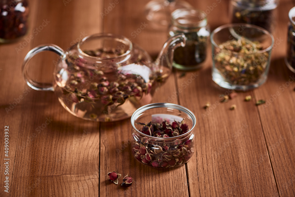 A jar of rose buds and a glass teapot on wooden table A jar of rose buds and a glass teapot on wooden table