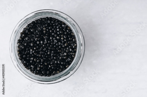 Black caviar in glass jar on white stone background