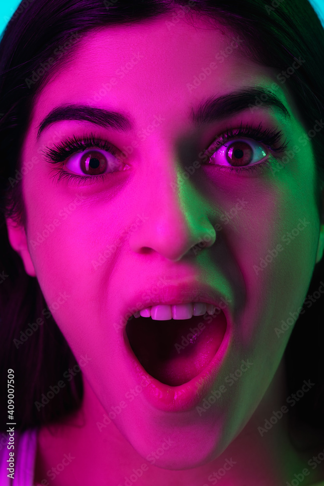 Shocked. Close up brunette woman's portrait isolated on blue studio background in mixed neon light. Beautiful female model. Concept of human emotions, facial expression, sales, ad, fashion. Beauty.
