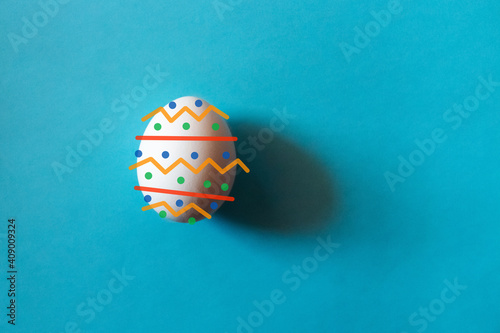 Easter concept. Painted one white egg isolated on color light blue pastel background.