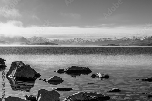 A misty winter day at the Lake Tekapo on New Zealand‘s South Island, snow-capped mountains, the Southern Alps, in the distance; black and white.