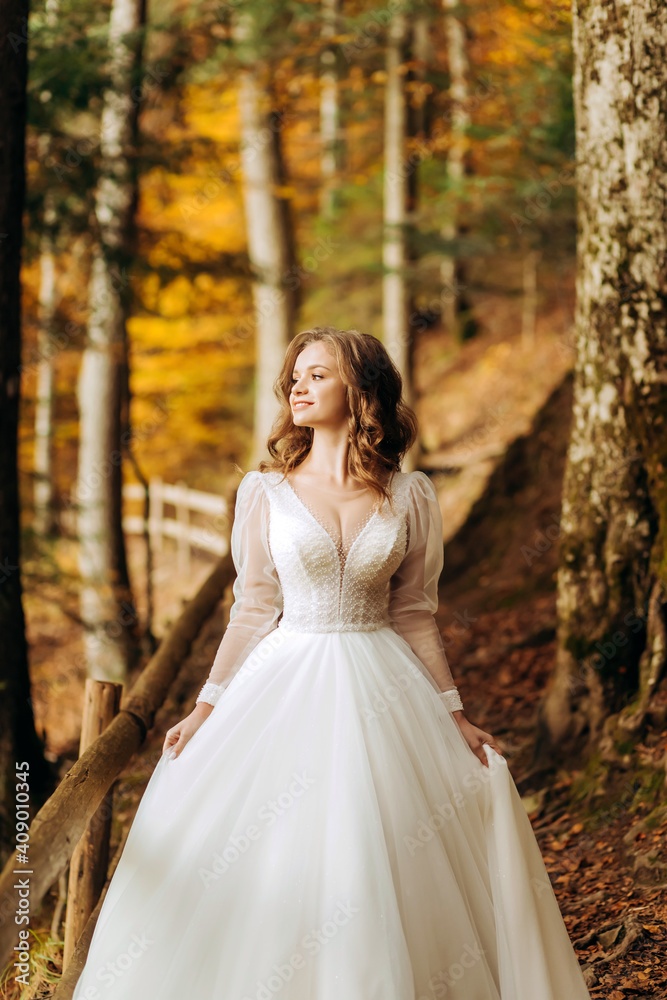 Amazing bride with wavy hair walks on a trail in autumn park.