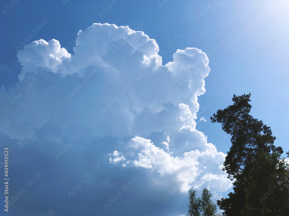 Powerful cumulus cloud illuminated by the sun on a blue sky in a forest park and on a hot summer day Powerful cumulus cloud illuminated by the sun on a blue sky in a forest park and on a hot summer day