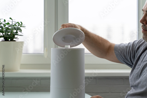 a man opens the lid of a humidifier to fill it with water. using a humidifier at home