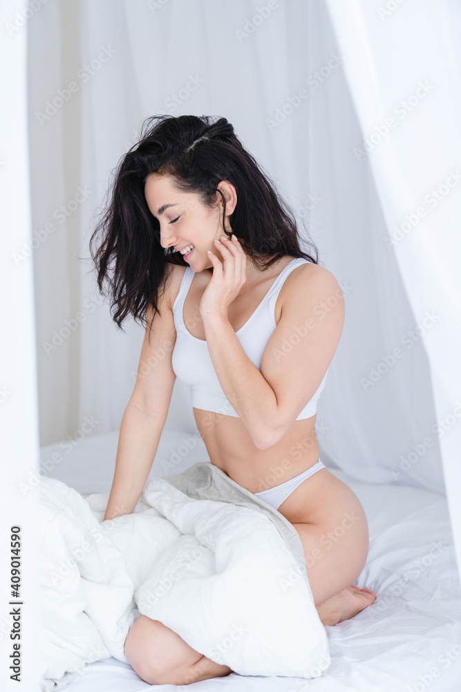 Vertical portrait of a young shy woman in underwear sitting on the bed Vertical portrait of a young shy woman in underwear sitting on the bed