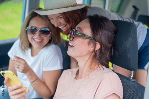 Three happy girlfriends go on a trip. Women Ride in the car, look at the phone and laugh. © Михаил Решетников