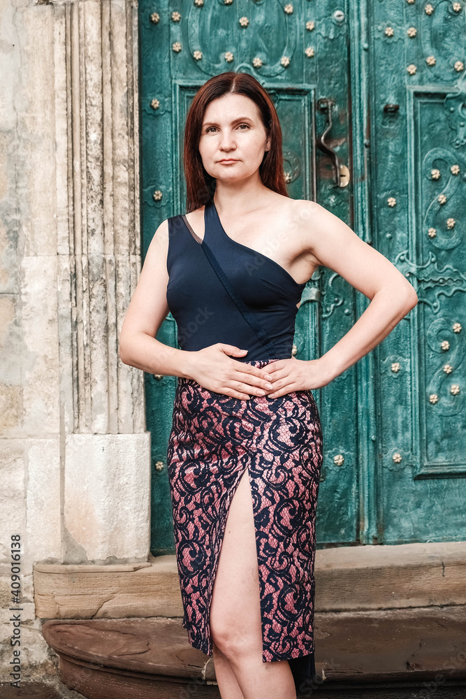 Fototapeta premium Beautiful woman in a sexy dress stands on the stairs on the background of an old house. Copy, empty space for text