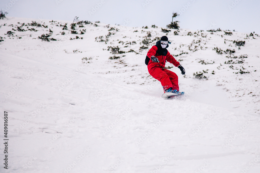 A guy in a red jumpsuit eating freeride on a snowboard on a snowy slope