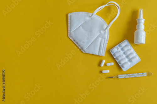 FFP3 mask, nasal drops, thermometer, tablets, various medicines lie on the table, top view, on a yellow background