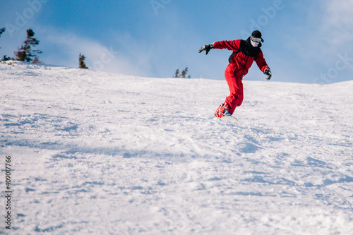 A guy in a red jumpsuit eating freeride on a snowboard on a snowy slope