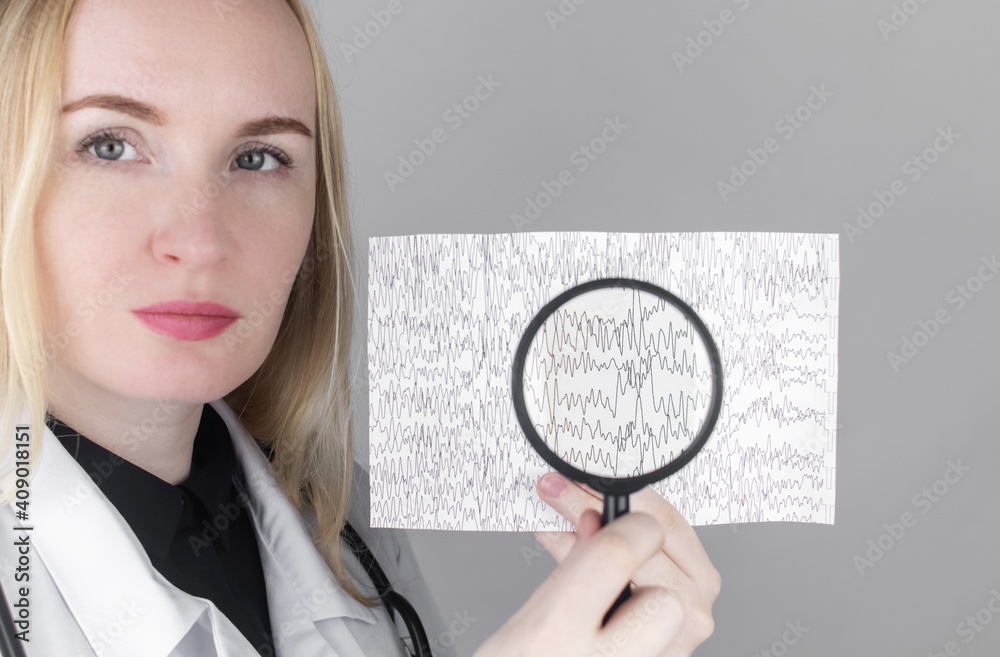 A neurologist with a magnifying glass examines an encephalogram of a patient’s brain. Schedule of electroencephalograms - study of brain currents for signs of epilepsy and pathologies A neurologist with a magnifying glass examines an encephalogram of a patient’s brain. Schedule of electroencephalograms - study of brain currents for signs of epilepsy and pathologies