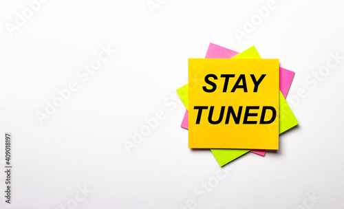 On a light background - bright multicolored stickers with the text STAY TUNED. Copy space