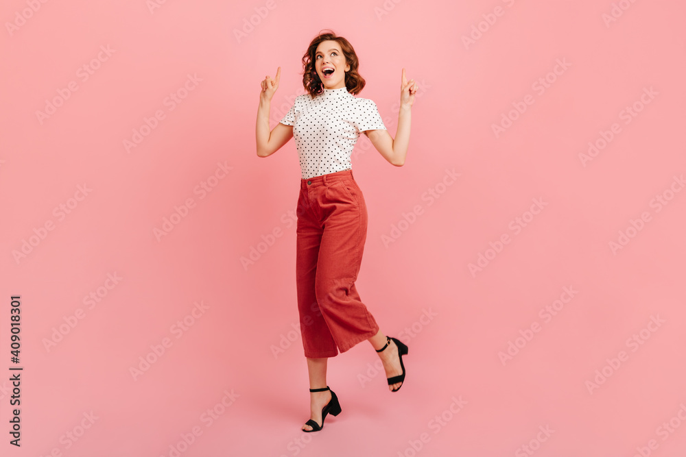Gorgeous girl in black shoes dancing in studio. Glad curly lady pointing with fingers up. - obrazy, fototapety, plakaty 