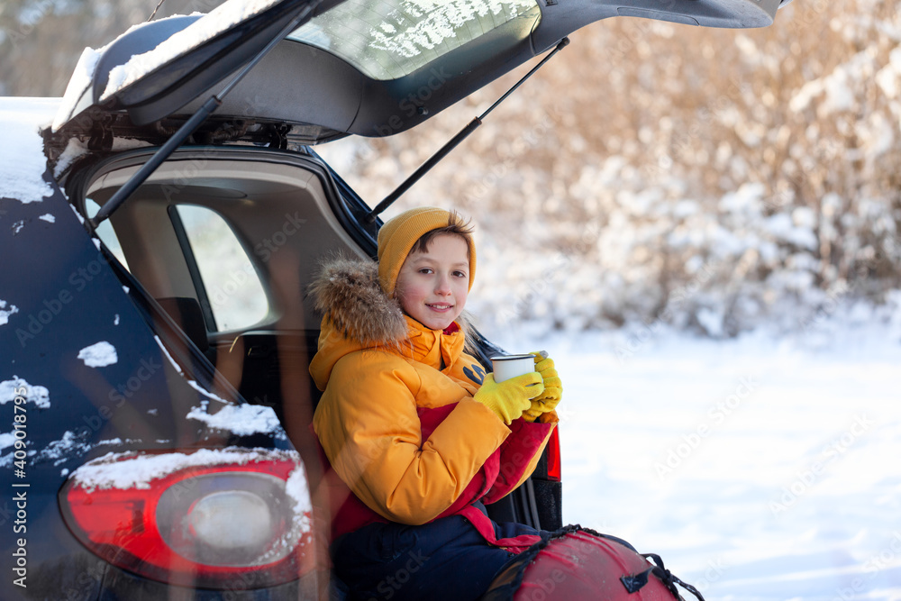 Child drinking hot chocolate or cocoa in sitting in black car at snowly winter day. Staycation, travel, tourism at winter time