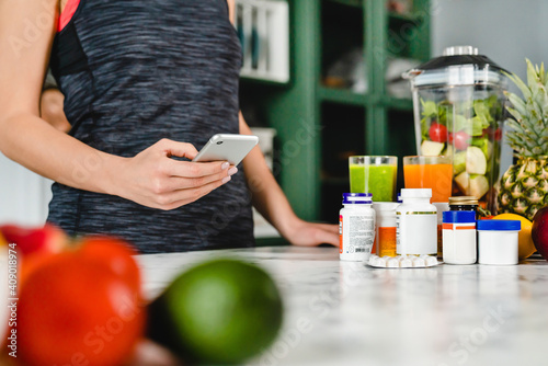 Young woman searching info about food supplements on her phone with fruits and additives on the table