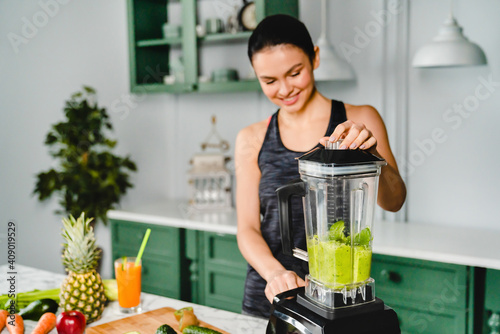 Фотография Cheerful young woman making smoothie using blender in the kitchen