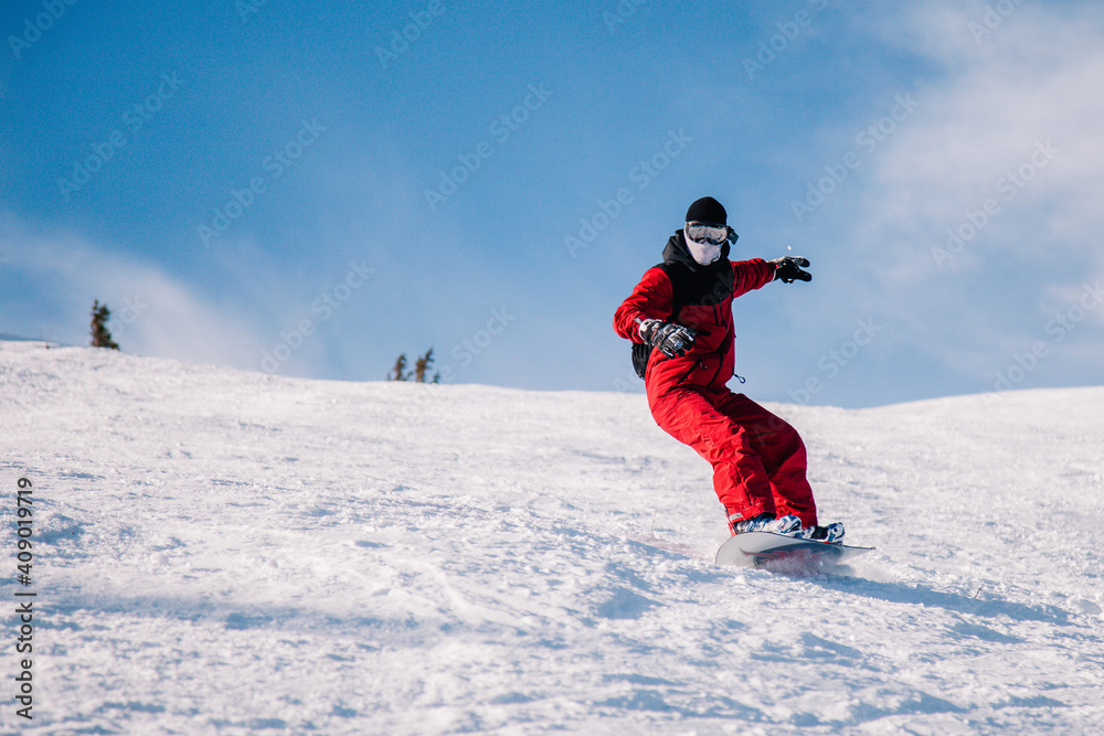 A guy in a red jumpsuit eating freeride on a snowboard on a snowy slope A guy in a red jumpsuit eating freeride on a snowboard on a snowy slope