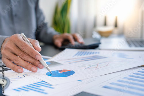 Finance business people or accountants point to the graph and use a calculator to calculate company income, expenses, taxes, and employee bonuses for Next year's improvement plan