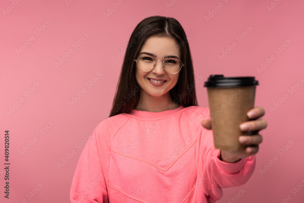 Photo of attractive woman in glasses holds coffee and takes selfie. Student wears casual pink t-shirt white pants isolated pink color background Photo of attractive woman in glasses holds coffee and takes selfie. Student wears casual pink t-shirt white pants isolated pink color background