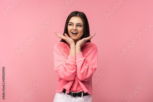 Photo of attractive woman in glasses smile surprised and wonder wear casual pink t-shirt white pants isolated pink color background © Ivan