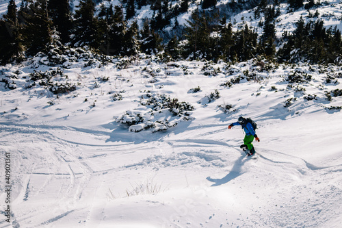 A guy in a bright suit rides a freeride on a snowboard on a snowy slope