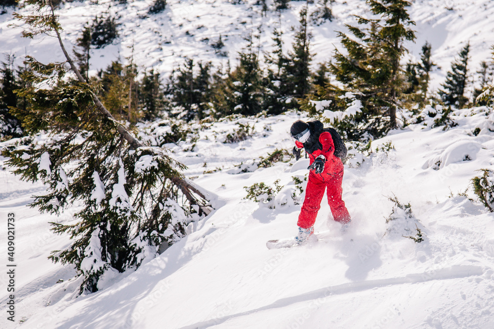 A guy in a red jumpsuit eating freeride on a snowboard on a snowy slope A guy in a red jumpsuit eating freeride on a snowboard on a snowy slope