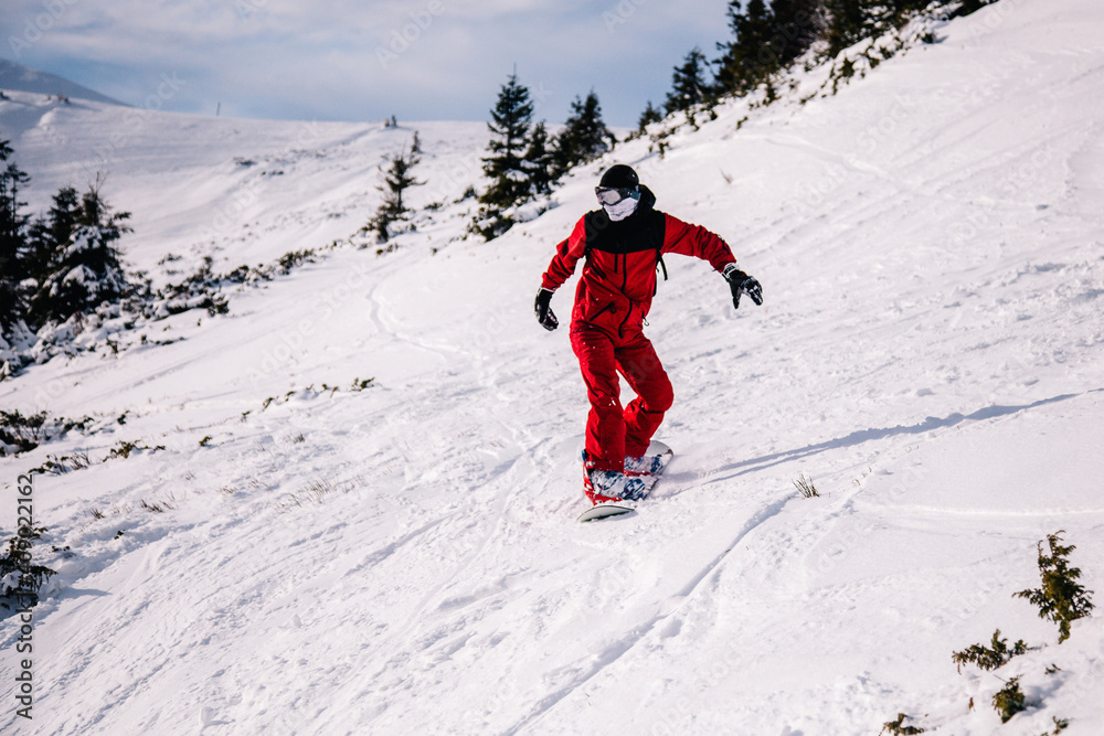 A guy in a red jumpsuit eating freeride on a snowboard on a snowy slope