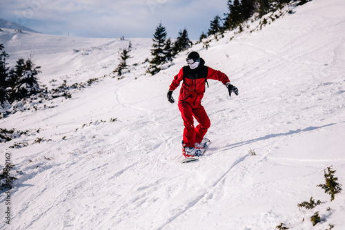 A guy in a red jumpsuit eating freeride on a snowboard on a snowy slope