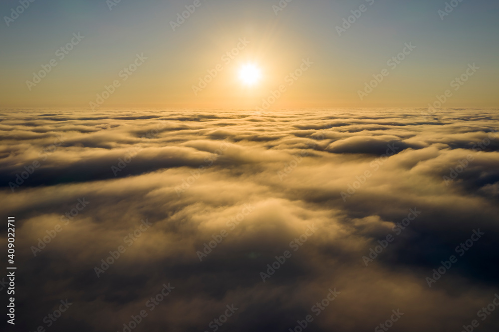 Striking aerial view of the sunset sky with the clouds below us. The shadows projected from the Sun passing through the clouds create a dramatical landscape view. Flying above the clouds in the search