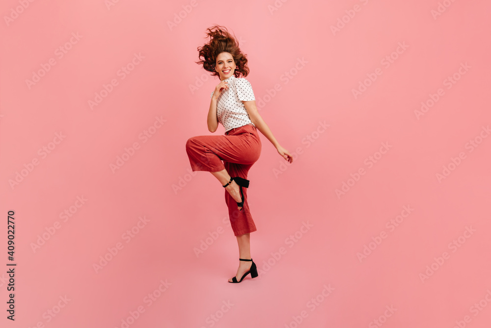Full length view of positive european girl in pink pants. Happy young woman dancing in studio.