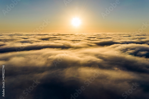 Striking aerial view of the sunset sky with the clouds below us. The shadows projected from the Sun passing through the clouds create a dramatical landscape view. Flying above the clouds in the search