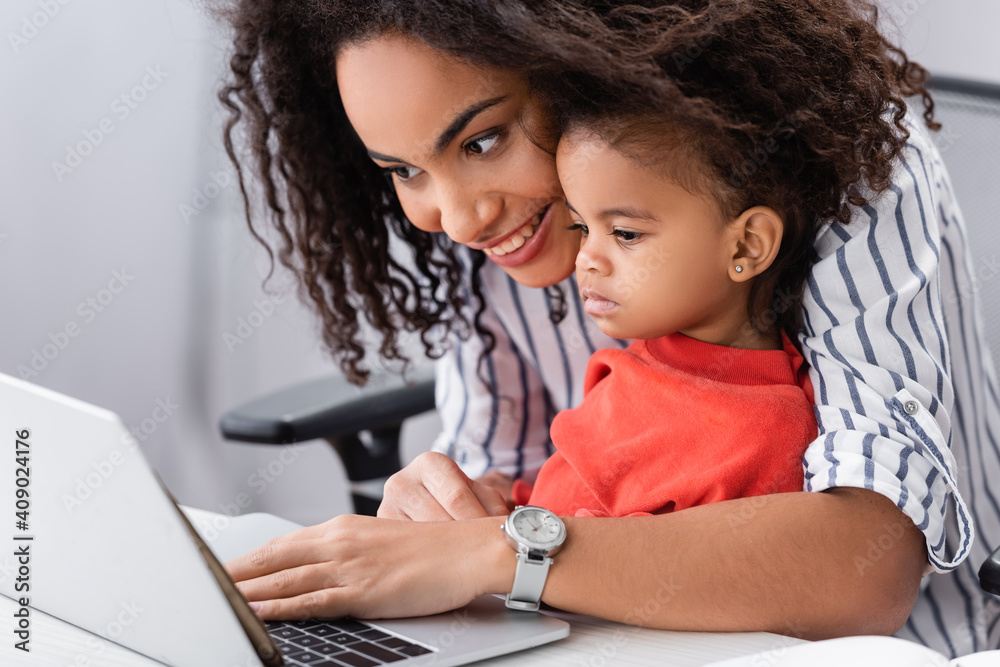 happy african american mother looking at laptop with toddler daughter happy african american mother looking at laptop with toddler daughter