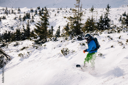 A guy in a bright suit rides a freeride on a snowboard on a snowy slope