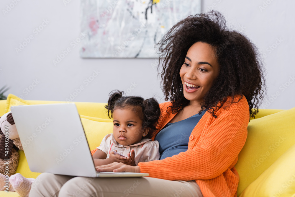 happy african american freelancer using laptop near toddler daughter in living room