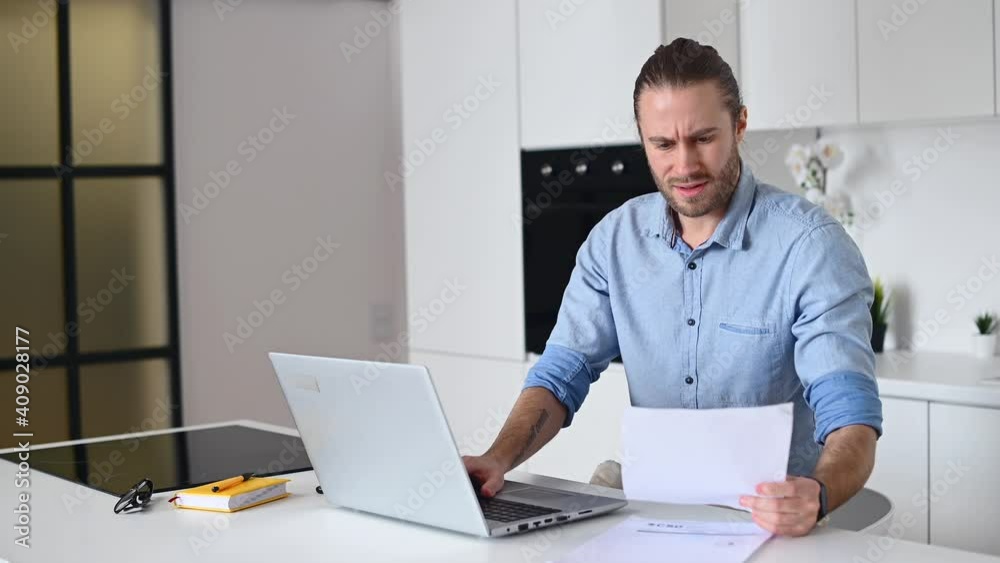The guy is discontented with the result of the work, crumples and discards the paper sheet sitting at kitchen countertop and working remotely with a laptop. Freelancer disagree with a technical task