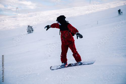 A guy in a red jumpsuit eating freeride on a snowboard on a snowy slope