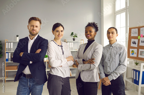 Portrait of confident company employees gathered together and posing for group photo. Team of happy young diverse business people standing in cozy modern office, smiling and looking at camera