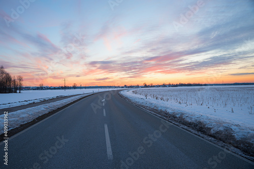 country road with curve in winter landscape, dreamy sunset sky, Brunnthal village, upper bavaria